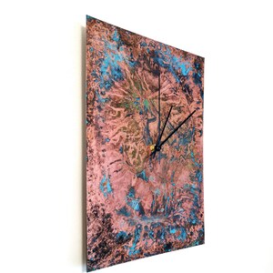 May include: Square copper wall clock with a distressed, blue and pink patina finish. The clock has black hands and a gold center.