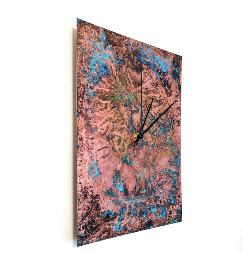 May include: Square copper wall clock with a distressed, blue and pink patina finish. The clock has black hands and a gold center.