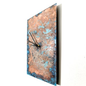 May include: A square copper clock with a blue and brown marbled design. The clock has black hands and a gold center.