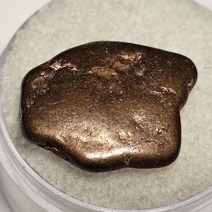 May include: A large, irregularly shaped piece of raw copper with a reddish-brown color. The copper has a rough, textured surface.