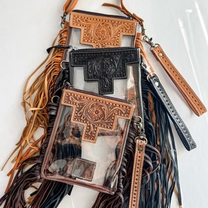May include: Three clear crossbody bags with brown leather fringe and tooled leather accents. The bags have a clear plastic front and a brown leather back. The bags are stacked on top of each other.