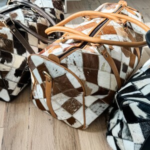 May include: Three brown, black and white patchwork leather travel bags with brown leather handles.