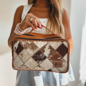 May include: A rectangular brown and tan cosmetic bag with a patchwork design. The bag features a leather handle and trim, a zipper closure, and a "Boho Ranch Shop" logo patch.