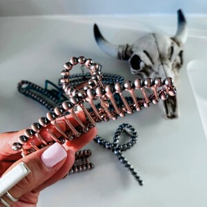 May include: A large, rose gold hair claw with a beaded design. The claw is made of metal and has a smooth, shiny finish.