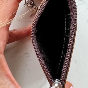 May include: A brown leather key chain with a zippered pouch and a metal key ring. The pouch is open and the zipper pull is visible.