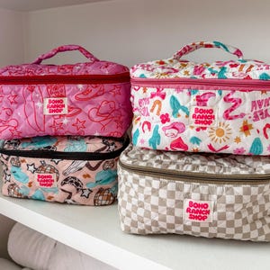 May include: Four quilted cosmetic bags in various patterns and colors. The bags feature a top handle, zipper closure, and the text "BOHO RANCH SHOP". Designs include pink with cowboy boots, white with horseshoes, and checkered beige.