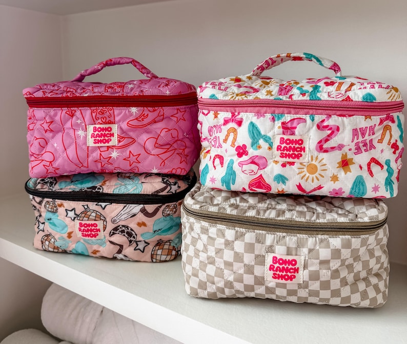 May include: Four quilted cosmetic bags in various patterns and colors. The bags feature a top handle, zipper closure, and the text "BOHO RANCH SHOP". Designs include pink with cowboy boots, white with horseshoes, and checkered beige.
