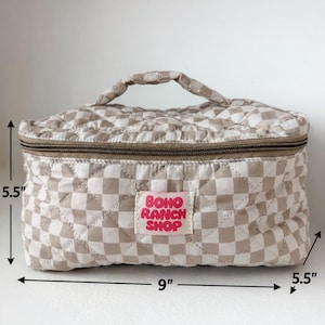 May include: A beige and white checkered quilted cosmetic bag with a top zipper and a handle. The bag is 9 inches wide and 5.5 inches high and deep. The label reads "Boho Ranch Shop" in pink text.