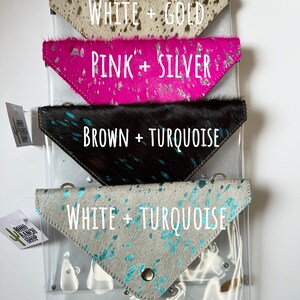 May include: Four triangular cowhide pouches with metallic finishes. The top is white and gold, the second is pink and silver, the third is brown and turquoise, and the bottom is white and turquoise. Each pouch features a snap closure and metal hardware.
