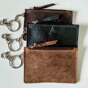 May include: Three leather keychains with zippered pockets and attached key rings. The keychains are brown, black, and dark brown.