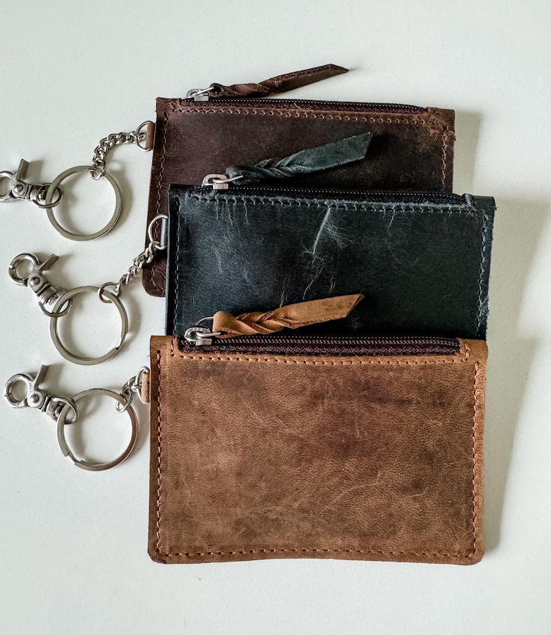 May include: Three leather keychains with zippered pockets and attached key rings. The keychains are brown, black, and dark brown.