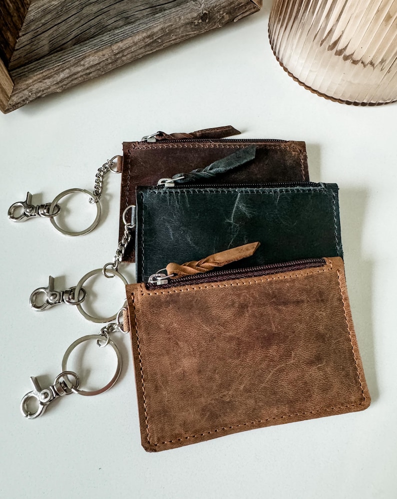 May include: Three leather keychains with zipper closures and key rings. The keychains are brown, dark green, and black.