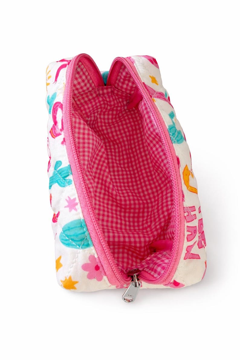 May include: A white quilted zippered pouch featuring a colorful print of cacti, flowers, and stars. The interior is lined with a pink and white gingham fabric. The pouch has a bright pink zipper closure and a silver metal zipper pull tab.