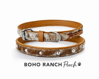 May include: Two dog collars. The top collar is light brown leather with a silver buckle and a section of cowhide. The bottom collar is brown cowhide with silver studs. The text "BOHO RANCH Pooch" is at the bottom.
