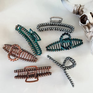 May include: Six hair clips with a beaded design. The clips are in various colors, including silver, copper, and green.