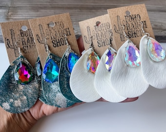 May include: Three pairs of dangle earrings with iridescent teardrop crystals and leather accents. The leather is in teal, white, and white. The earrings are labelled "Boho Ranch Shop".