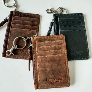 May include: Three leather card holders with zipper closures and keychains. The card holders are brown, black, and dark green. Each card holder has the text "BOHO RANCH handmade" embossed on the front.