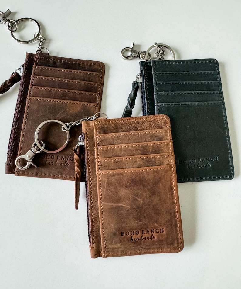 May include: Three leather card holders with zipper closures and keychains. The card holders are brown, black, and dark green. Each card holder has the text "BOHO RANCH handmade" embossed on the front.