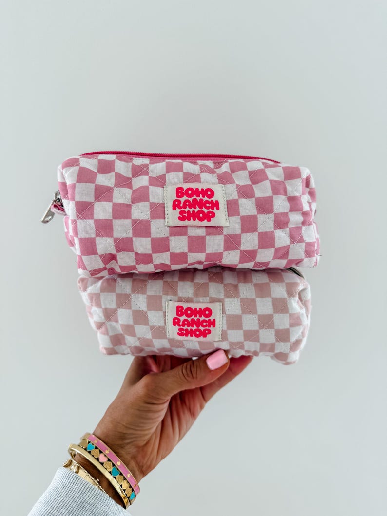 May include: Two stacked rectangular quilted pouches featuring a pink and white checkered pattern. Each pouch has a central white fabric label with the text BOHO RANCH SHOP printed in bold pink letters. The pouches include a pink zipper closure.