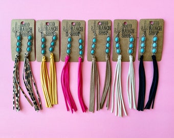 Puede incluir: Ocho pares de pendientes colgantes de turquesa y plata con borlas de gamuza en varios colores, incluyendo estampado de leopardo, amarillo, rosa, marrón, blanco y negro. Los pendientes se muestran en tarjetas marrones con el texto "BOHO RANCH SHOP".