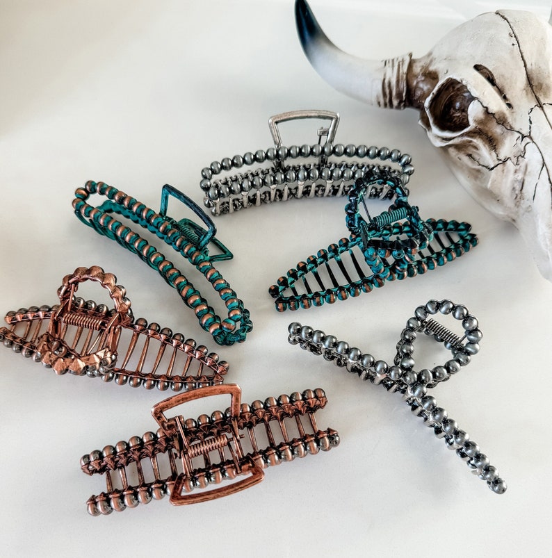 May include: Five different hair clips in various colors and styles. The clips are made of metal and have a beaded design. The clips are arranged on a white surface.