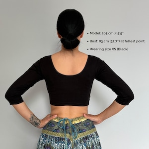 May include: A black, three-quarter sleeve crop top with a scoop neckline. The model is wearing size XS. The bust measurement is 32.7 inches. The model is 5'5" tall. The top is a solid black color.