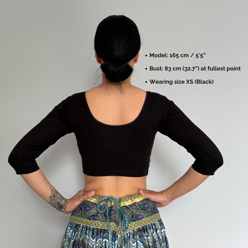 May include: A black, three-quarter sleeve crop top with a scoop neckline. The model is wearing size XS. The bust measurement is 32.7 inches. The model is 5'5" tall. The top is a solid black color.