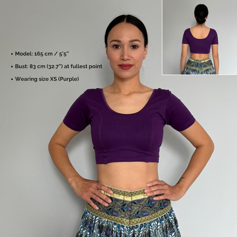 May include: A cropped, short-sleeved purple top with a scoop neckline. The model is wearing size XS. The image also includes a smaller image of the back of the top. The model's bust is 32.7 inches at the fullest point.