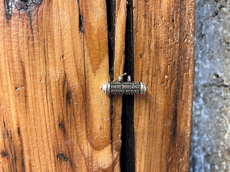 Pode incluir: Um bracelete de prata com um pequeno amuleto cil&iacute;ndrico que diz "Hare Krishna Hare Krishna Krishna Krishna Hare Hare".