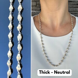 Puede incluir: Un collar de plata con peque&ntilde;as cuentas redondas. El collar es grueso y tiene un color neutro. El texto "Thick - Neutral" est&aacute; impreso debajo del collar.