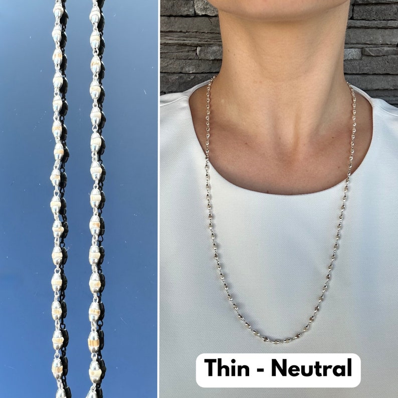 Puede incluir: Un collar de cadena de plata con peque&ntilde;os eslabones ovalados. El collar es fino y tiene un color neutro. El texto "Thin - Neutral" est&aacute; impreso debajo del collar.