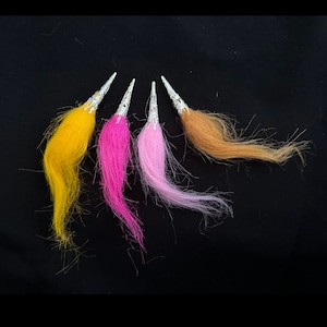 May include: Four decorative hair clips with colorful feathered tails. The clips are silver with a decorative design and the feathers are yellow, pink, light pink, and brown.