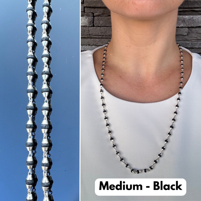 Puede incluir: Un collar de cuentas plateadas y negras de longitud media. El collar lo lleva una persona con una camisa blanca. El texto "Medium - Black" es visible en la parte inferior de la imagen.