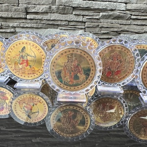 Könnte beinhalten: Eine Sammlung runder, goldfarbener Dekorplatten mit Bildern von hinduistischen Gottheiten. Die Platten sind in klarem Kunststoff gerahmt und haben einen dekorativen Rand.