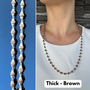 Puede incluir: Un collar marr&oacute;n y plateado con cuentas redondas gruesas. El collar est&aacute; sobre una camisa blanca y el texto "Thick - Brown" est&aacute; debajo del collar.