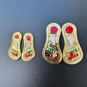 Könnte beinhalten: Vier goldfarbene Fuß-Anhänger aus Metall mit roten und grünen Emaille-Akzenten. Die Anhänger sind mit weißen und roten Edelsteinen verziert.