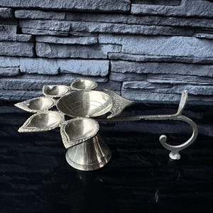 May include: A brass diya with five wicks, a handle, and intricate floral designs. The diya is a traditional Indian oil lamp used for religious ceremonies and festivals.