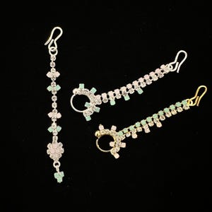 May include: Three silver and gold nose rings with rhinestones. The rings are decorated with clear and green rhinestones.