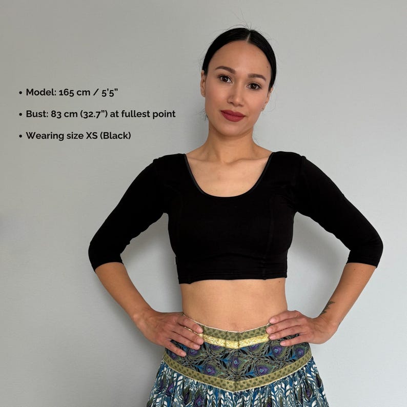 May include: A black, three-quarter sleeve crop top with a scoop neckline. The model is wearing size XS. The image also includes the model's height of 5'5" and bust measurement of 32.7 inches.