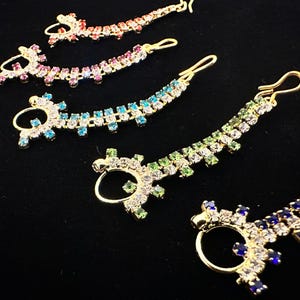 Op de afbeelding: Vijf gouden neusringen met heldere en gekleurde strasssteentjes. De ringen zijn in verschillende kleuren: roze, blauw, groen en blauw.