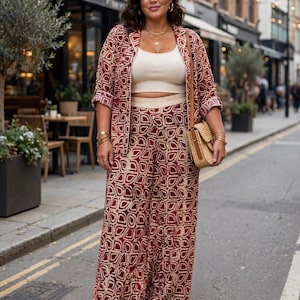 May include: A matching two-piece set consisting of a long-sleeved blazer and wide-leg trousers, both featuring a dark red and beige geometric pattern. The outfit is paired with a cream-colored cropped tank top and a small woven straw shoulder bag.