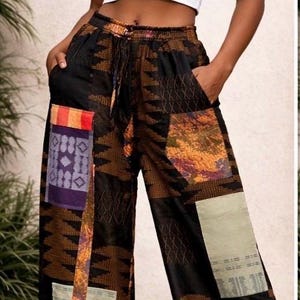 Puede incluir: Pantalones anchos de patchwork con un patrón geométrico negro y marrón, con parches de tela coloridos. Los pantalones tienen cintura con cordón y bolsillos. La modelo lleva un top corto blanco.