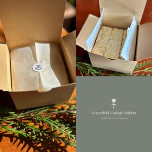 May include: Two open cardboard boxes of Scottish shortbread. One box contains a wrapped block of shortbread with a thistle sticker. The other box contains several shortbread biscuits. The Greenfield Cottage Bakery logo is visible.