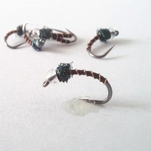 May include: Close-up of four dark green and silver fly fishing lures with copper wire wrapped around the hooks.
