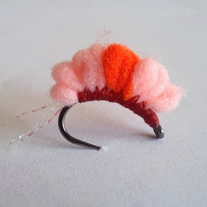 May include: A pink and orange fly fishing lure with a red thread body and a silver hook.