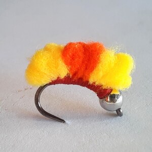 May include: A yellow and orange fly tying material with a silver bead head.