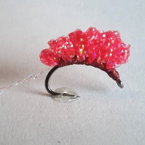 May include: A red and iridescent fly fishing lure with a clear tail.