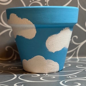 May include: A blue terracotta planter with white painted clouds. The planter is a simple, round shape with a slightly flared rim.
