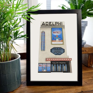 May include: A framed illustration of the Adelphi Theatre in New York City, featuring a white building with red accents and a large sign that reads "WAITRESS".