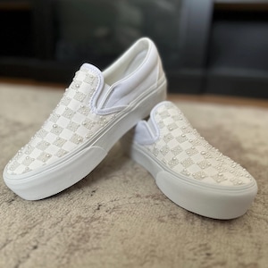 Könnte beinhalten: Weiße Vans Slip-on Sneaker mit einem karierten Muster, das mit weißen Perlen bedeckt ist.